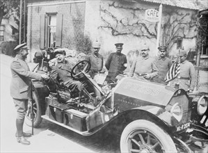 Cigar Chomping War Correspondent shakes hands with a Military person in Germany while sitting in his large limousine marked Press on the Hood in large letters; on looking military personnel are in fro...