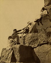 Egyptian men assisting a tourist who is attempting to climb the Great Pyramid of Cheops. 1880