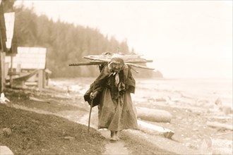 Elderly Makah woman carrying faggots, a bundle of sticks, on her back, at Neah Bay, Washington 1911
