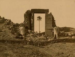 Entrance to the remains of the Temple of Aménophis flanked by headless statues of Ramses in Thebes. 1880