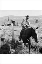 Cowboy holds his baby while riding a horse 1939