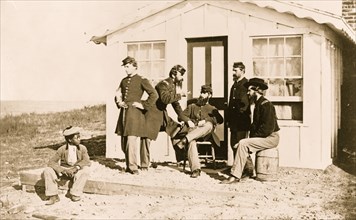Five Civil War soldiers gathered on dirt porch outside home, African American youth seated near them 1863