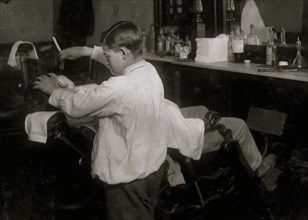 A 12-year old barber lathers and shaves customers in father's shop 1917