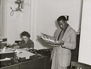 Gordon Parks, Farm Security Administration/Office of War Information photographer, standing in office with Helen Wool seated at desk 1943