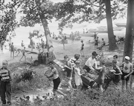 Group of Boys carry loaves of bread from wagons near beach front in woods. 1923