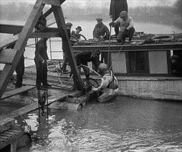 Helmeted and Oxygen tubed divers is ready to submerge to Investigate an auto wreck 1923