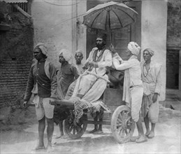 Hindu Priest conveyed on a Two-Wheeled Cart as an attendant holds an umbrella over the cleric's head. 1912