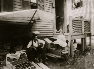 Fruit Vendor sells sooty Product; Mother and Daughter work with Father outside their home 1912