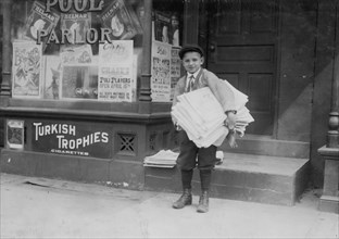 Hyman Lapcoff,  a ten year old Newsie from a good family, carrying a heavy load of newspapers quite a distance. He sells outside of a pool Hall. 1912