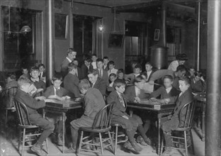 In the Newsboys Reading Room. Boys seated at tables playing gamers. 1909