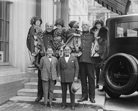 Little People all dressed in their finery are lifted in the arms of full sized people. 1924