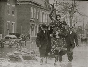Man carries and woman over flooded streets; he has two male companions 1924
