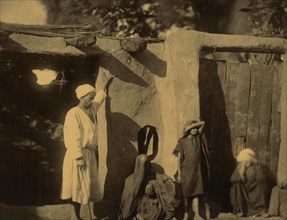 Man, woman, and children outside earth and wood structure 1880