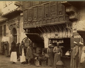 Men standing next to shop stall open to street, 1870