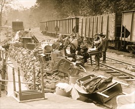Men women and children flood victims pile up their home belongings to try to save them. They are all a train railroad signing with coal cars behind them and an embankment of a stream in front 1924