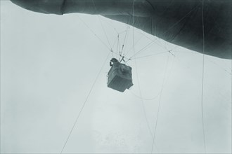 Military Observer hangs from a Balloon by guide wires looking over battlefield