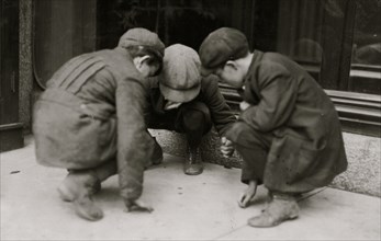 Mill boys pitching pennies on the Main St. in the afternoon.  1916