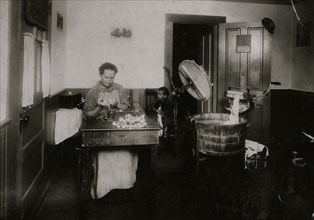 Putting the bristles into tooth brushes in the kitchen of a home.  1912