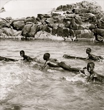Nubian boys shooting the rapids of the Nile on logs, Egypt 1901