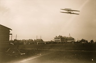 Orville Wright flying in his airplane, crowd on field 1908