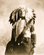 Plenty Holes, a Sioux Indian in feather headdress and bone breast piece,  1900