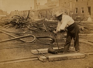Railroad construction worker straightening track; pile of twisted rails in background. 1862-63 1863