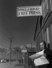 Roy Takeno reading paper in front of office 1943