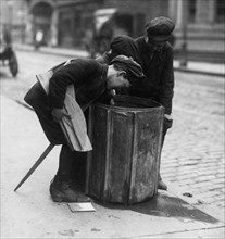 Scavengers pull fire wood from a waste basket 1916