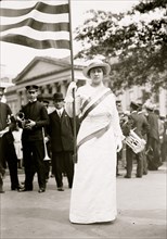 Suffragette holds flag at the head of a waiting male band 1913