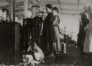 Knitter is a little girl so small she has to stand on a box to reach her machine. 1910
