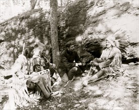 three Blackfeet Indians, demonstrating how to start a fire using a bow and a stick, rocks and trees in background 1917