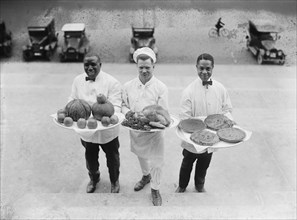 Three Chefs stand on bottom of a line of steps and hold up Thanksgiving platters of Pies, apples and a Turkey 1922