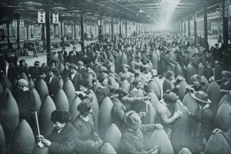 Throngs of women interspersed amongst large artillery shells on a factory floor. 1917