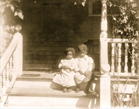 Two African American children sitting on steps to porch 1899
