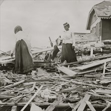 Two African American women search through rubble following a violent hurricane which devastated most of Galveston and took more than 5,000 lives. 1900