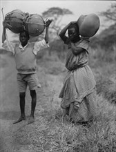 Uganda boy and girl carrying jars 1936