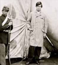 Washington Navy Yard, District of Columbia. Lewis Payne, standing in overcoat and without hat. Federal guard standing on left 1865