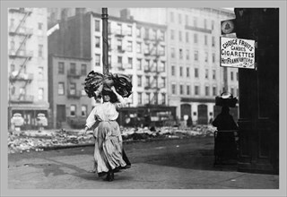 Immigrant Woman Walks Down Street Carrying a Pile of Clothing on Her Head 1900