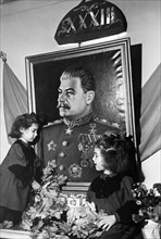 Two young girls at a kindergarten in the sverdlov district of moscow adorning a portrait of joseph stalin with greenery on the eve of the 33rd anniversary of the great october socialist revolution, no...