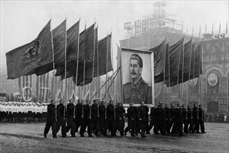 A demonstration / parade of the working people in red square in moscow on november 7, 1950, the sportsmen are carrying soviet flags and an image of stalin.