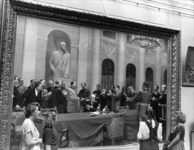 Visitors examining the painting 'in the name of peace' by soviet artists v, vikhtinsky, b, zhukov, e, levin, l, chernov, and l, shmatkov at the exhibition of ukrainian fine arts in the tretyakov galle...