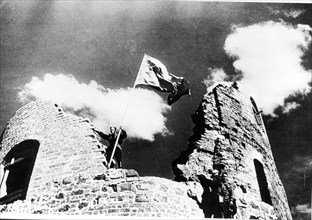 Once more the red flag of the ussr flutters in the wind as a red army fighter unfurls it over the old kaunas fortress.
