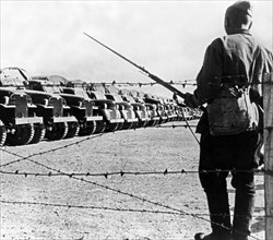 A soldier standing guard over a long line of american trucks at a lend-lease depot in iran, the trucks arrived and were assembled in the persian port and are now awaiting shipment to the soviet union.