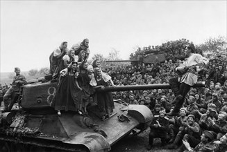 A t-34 tank provides a suitable stage, at the front, for a group of kiev entertainers performing for the troops of the 3rd ukrainian front during world war ll.