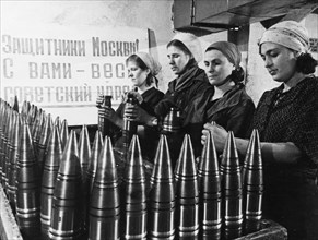 Civilian women making artillery shells at a munitions factory in moscow during world war 2, the sign behind them reads: 'defenders of moscow! the soviet people are with you!'.