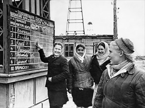 A crew of young women workers, headed by mari volkova (right), have just finished their shift and are reading the results of the high output competition, volkova and her girlfriends are in second plac...