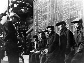 Workers studying diagrams indicating the output accomplished at the blast furnace shop of the magnitogorsk iron and steel works.