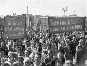 Berlin, gdr, may 1, 1957, berlin's working people marching across marx-engels square, the banners read 'we demand that atomic weapons be prohibited and outlawed!' (left) and 'forward with the building...