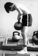 A young boy at the sambo-70 sports school lifting weights as he trains to be a sambo wrestler, russia, 1991.