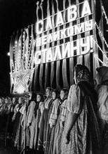 An amateur folk chorus singing in manezh square in moscow on the occasion of j,v, stalin's 70th birthday, december 21, 1949, 'glory to the great stalin' written in lights behind them.